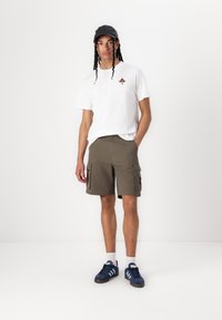 T-shirt en coton blanc avec un petit motif brodé, shorts cargo olive, baskets bleu foncé avec des rayures bleu clair, casquette noire.