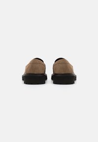 Chaussures slip-on en suede marron avec un dos arrondi, une tige texturée et une épaisse semelle en caoutchouc noir, conçues pour le confort et la facilité d'enfilage.