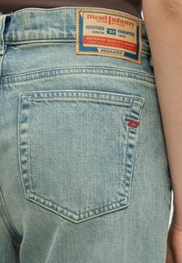 Vaqueros de mezclilla azul claro con una etiqueta de parche en la pretina con detalles en rojo y azul, y un bolsillo trasero con un sutil detalle de costura.