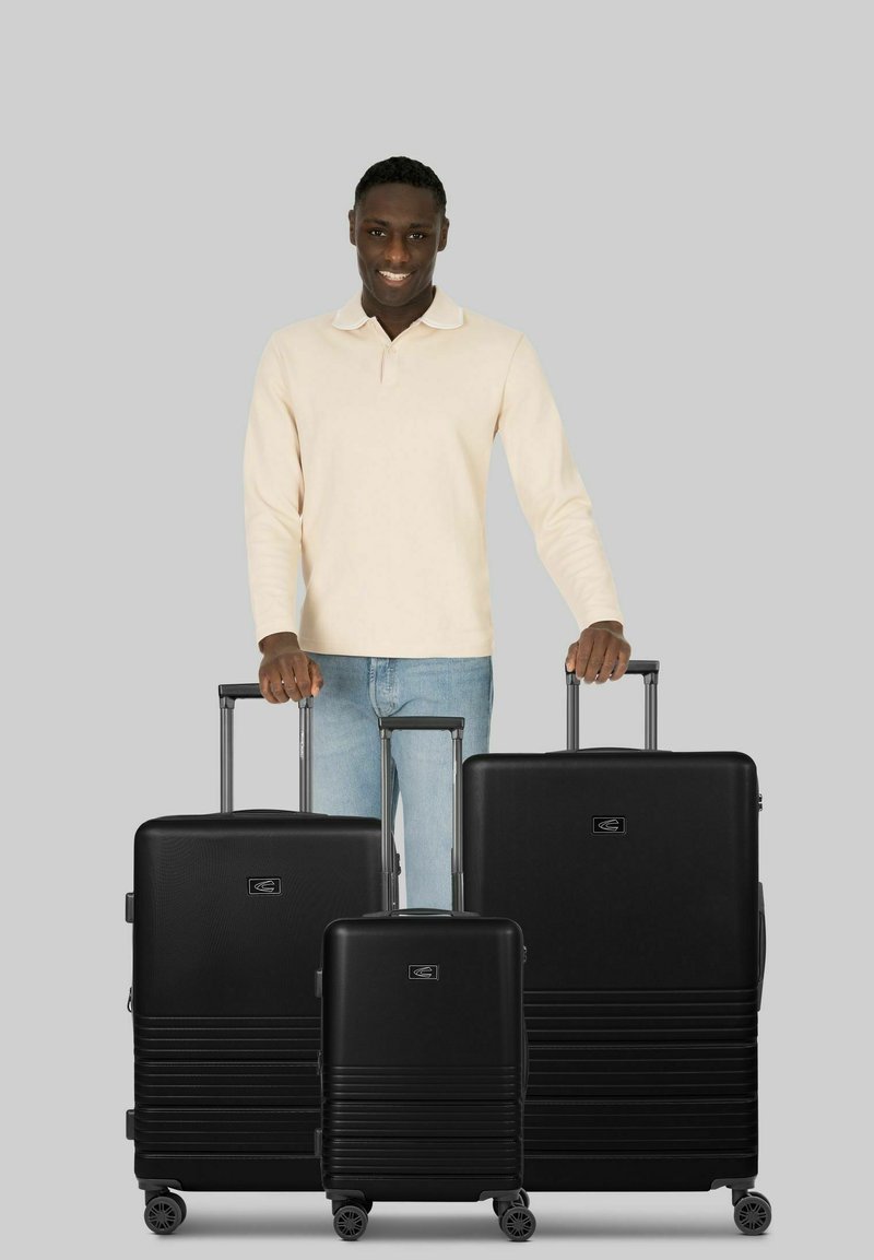 Ensemble de valises rigides noires composé de trois tailles, présentant des motifs texturés verticaux et des poignées télescopiques avec des roulettes.