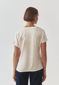 Light beige silk blouse with short sleeves, round neckline, and a slightly curved hem. Smooth texture with minimal design details.