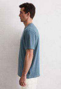 Helles blaues T-Shirt mit kurzen Ärmeln, Rundhalsausschnitt, weichem Baumwollstoff, lockere Passform, seitliche Schlitze, getragen mit beigen leichten Hosen.
