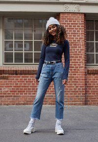 Dlouhý rukáv námořnický top s logem "Levi's California", oprané světlé modré džíny, bílé vysoké tenisky a šedý pletený čepice.