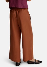 Kalhoty s širokým střihem v rustové barvě z texturované tkaniny, s elastickým pasem a bočními kapsami, doplněné černými síťovanými balerínami.