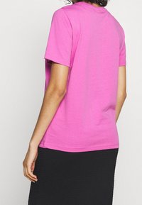 Tričko s krátkým rukávem, kulatým výstřihem z jasně růžové bavlny. Hladká textura, rovný střih a obšité lemy. Nosené s černou sukní.