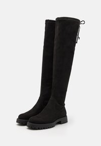 Botas de ante negras hasta la rodilla con suela plana estriada y lengüeta. El diseño elegante presenta una parte superior sin costuras y detalles de costura mínimos.