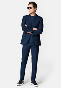 Granatowy garnitur z dopasowaną marynarką, pasującymi spodniami slim-fit oraz granatowym t-shirtem. Uzupełniony ciemnymi okularami przeciwsłonecznymi i casualowymi sneakersami.