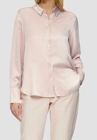 Camicia di satin rosa chiaro con colletto a punta, maniche lunghe e chiusura con bottoni. Tessuto liscio e design dell'orlo leggermente curvato.