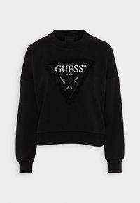 Sudadera negra con diseño recortado, cuello redondo y mangas extragrandes. En la parte frontal presenta un logo triangular texturizado con detalles de marca.