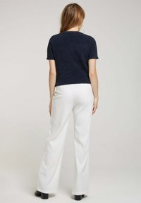 Haut en maille à manches courtes de couleur marine en tissu texturé, associé à un pantalon large blanc. Modèle vu de dos. Bottines noires visibles.