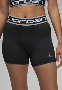 Crne atletske kratke hlače s kontrastnim sivim pojasom na struku i "Jordan" logotipom. Materijal je glatki i rastezljiv, s malim logotipom na bedru.