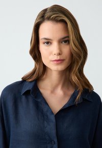 Camicia di lino blu navy con una texture morbida, chiusura frontale a bottoni e colletto classico. Presenta una vestibilità rilassata e una leggera lucentezza.