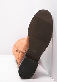 Botín de ante marrón claro con punta redonda suave, detalle de cremallera lateral y suela de goma negra con agarre texturizado. Talla 37 indicada.