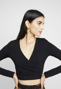 Top preto de manga longa cruzado com decote em V profundo, feito de tecido macio, combinado com calças de cintura alta com padrão. Design simples, forma ajustada.