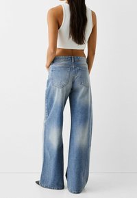 Helleblaue Weitbeine-Jeans mit einem ausgewaschenen Look, hoher Taille, fünf Taschen und einer klassischen Denim-Textur. Die Rückansicht zeigt die Details der Taschen.