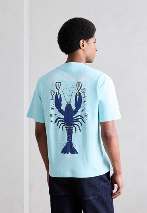 Άνδρας που φοράει φανέλα ανοιχτού μπλε χρώματος με μεγάλο σκούρο μπλε αστακό που κρατά ποτήρια κρασιού και το κείμενο «Dolce Vibes Only» στην πλάτη.