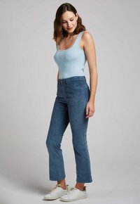 Débardeur côtelé bleu clair associé à un jean taille haute bleu foncé, avec une fermeture à boutons et des baskets blanches. Textures lisses et ajustées.