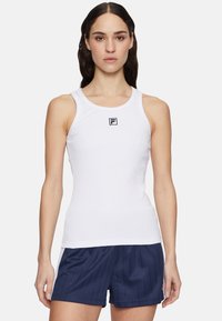 Canottiera bianca a coste con scollatura rotonda, caratterizzata da un piccolo logo nero al centro. Indossata con pantaloni corti a righe blu navy.