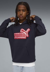 Sweat à capuche bleu marine en tissu doux, avec un logo Puma rouge bien visible, une poche kangourou et une capuche réglable à cordon.