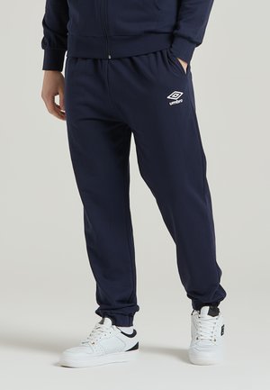 Pantaloni jogger navy realizzati in materiale morbido, con vita elasticizzata, polsini alle caviglie e un accento con logo bianco. Abbinati a sneakers bianche.