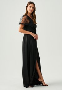 Long black dress with sheer, puffed sleeves featuring polka dots. The dress has a wrap design and a thigh-high slit for added detail.