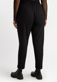 Pantalons de jogging noirs avec une taille élastique et des chevilles resserrées. Fabriqués dans un tissu doux, présentant une texture lisse et une coupe décontractée.