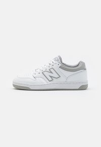 Białe i szare sneakersy New Balance z sznurowadłami, perforowanym przodem, wyściełanym kołnierzem i fakturowaną podeszwą, pokazane z boku na białym tle.