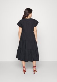 Black cotton tiered dress with short ruffled sleeves. Worn with red strappy heels. Simple, flowing design with a mid-calf length.