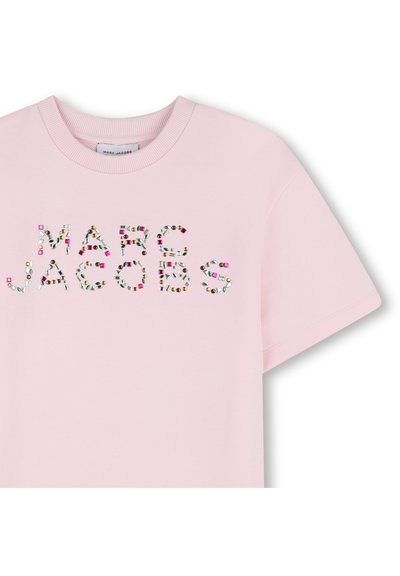 Ροζ ανοιχτό ροζ κοντομάνικο μπλουζάκι με πολύχρωμα διακοσμητικά γράμματα που σχηματίζουν το "MARC JACOBS" με διακοσμήσεις που μοιάζουν με πολύτιμους λίθους. Λείο ύφασμα.
