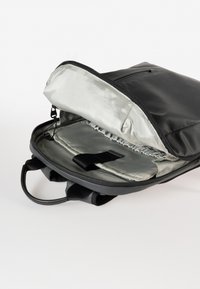 Zaino nero con apertura con cerniera, dotato di un esterno liscio e di un interno foderato in satin grigio chiaro. Include una tasca e un elastico.