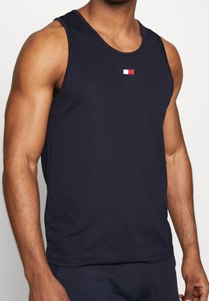 Muskelöser Mensch trägt ein dunkelblaues ärmelloses Tanktop mit einem kleinen roten, weißen und blauen rechteckigen Logo in der Mitte der Brust.