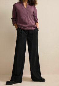 Blusa viola a maniche lunghe con colletto abbinata a pantaloni neri a strisce larghe. Scarpe nere con suola spessa completano l'outfit.