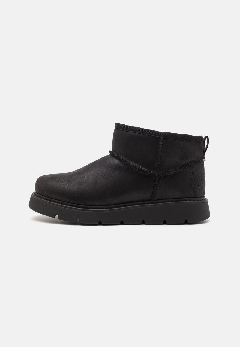 Bottine noire à cheville avec semelle épaisse et plate, talon avec languette de préhension, détails de coutures visibles, et finition matte lisse sur le dessus.