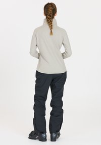 Lichtgrijze lange mouw top met een hoge kraag, gecombineerd met zwarte broek met ritsen bij de enkels. Zwarte laarzen met hardwaredetails.