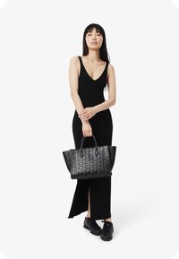 Abito nero a costine con scollatura a V profonda e spacco laterale. Tiene una borsa nera texture con dettagli geometrici. Sneakers nere completano il look.