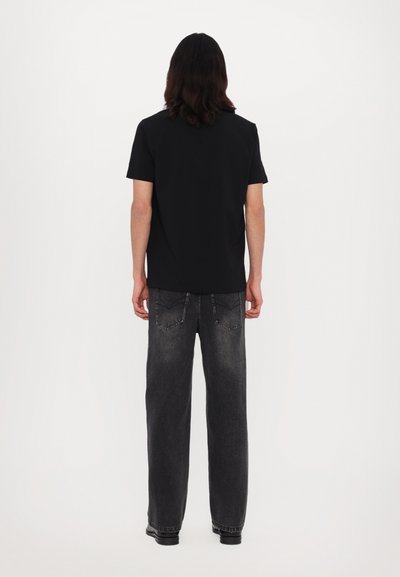 Sort kortærmet t-shirt parret med løstsiddende grå denim jeans. Bemærkelsesværdige detaljer inkluderer baglommer og en subtil falmning på jeansene.