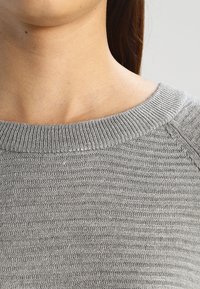 Grauer Strickpullover mit einem breiten, strukturierten Ausschnitt. Gerippte Details entlang der Kanten und ein glatter Körper. Weiches Material, lässige Passform.