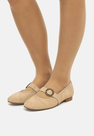 Bailarinas de ante beige Mary Jane con un tacón bajo, que presentan una hebilla circular acentuada y un ribete en contraste a lo largo de la abertura.