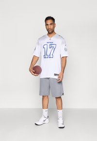 Bijela nogometna majica s plavim naglascima i brojem 17, uparena sa sivim hlačama. Bijele tenisice s crnim naglascima i visoke čarape.