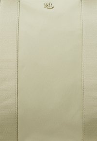 Pochette beige à la finition lisse et mate. Présente une bande verticale centrale et un petit logo en relief. Les bords sont dotés de coutures soignées.