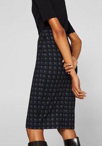 Marinblå midikjol med rutmönster, tillverkad av ett texturerat tyg. Har en figursydd silhuett och slutar strax under knäet.