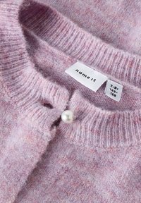 Gaiši violetā adīta jaka ar ribotu apkakli, ar pērļu pogu aizdari un etiķeti ar zīmola un izmēra informāciju.