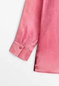 Chemise à manches longues rose avec un design dégradé ; texture lisse, poignet à boutons, ourlet légèrement arrondi, tissu léger.