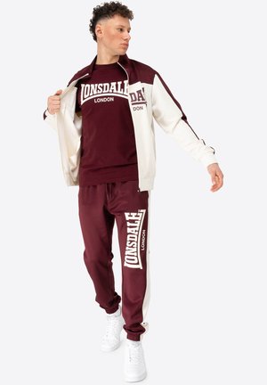 Training suit bordeaux cu accente albe; jachetă cu fermoar și pantaloni cu talie elastică. Include logo-ul "Lonsdale London" expus proeminent.