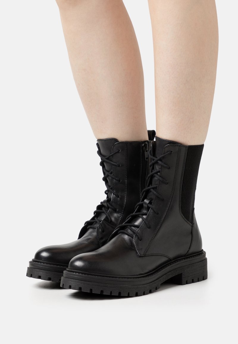 Czarne skórzane botki za kostkę z sznurówkami z przodu, zamkiem błyskawicznym z boku i akcentami z teksturowanej tkaniny. Gruba gumowa podeszwa z rowkami dla lepszej przyczepności.