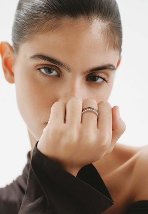 Anillo de plata con tres bandas, que presenta dos lisas y una adornada con pequeños acentos circulares, sobre un fondo neutro.