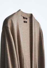 Cardigan beige con apertura frontale, realizzato in tessuto morbido. Caratterizzato da un ampio colletto e maniche lunghe, dettagli di cucitura minimi e senza chiusure.