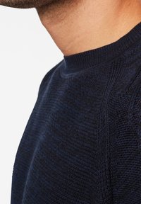 Marineblauer Pullover mit geribkeltem Rundhalsausschnitt, strukturiertem Strickmuster und Raglanärmeln, der feine Details im Stoff zeigt.