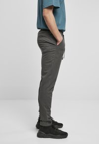 Pantalones grises de corte slim con cintura elástica, bolsillos laterales y un tejido texturizado; combinados con zapatillas deportivas negras.