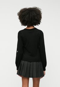 Suéter negro de punto con mangas largas abullonadas, dobladillo acanalado y escote redondo. Combinado con una falda gris con pliegues, que muestra un diseño limpio.